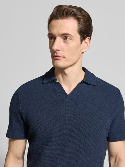 Męski model nosi Regular Fit Poloshirt aus Baumwoll-Mix od MCNEAL, mieszanka bawełny i elastanu, pika, wykładany kołnierz z dekoltem w serek, krótkie rękawy, długość tyłu 69 cm w rozmiarze M, granatowy, tekstura waflowa, z przodu, zbliżenie na górną część ciała.