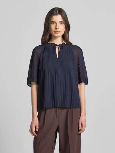 Kobiece modelka nosi Regular Fit Blusenshirt in Plissee-Optik von s.Oliver BLACK LABEL, efekt: jednolity kolor, krój regular fit, kształt kołnierza: kołnierz z falbanami, plisy, okrągły dekolt, wycięcie w kształcie łezki, wiązanie, rękaw: krótki rękaw, widok całej sylwetki z przodu.
