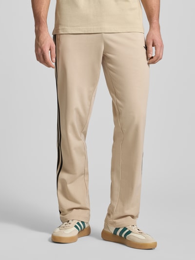 Männermodel draagt Heren Trainingshose met logoprint, model 'FIREBIRD' van adidas Originals, regular fit, elastische band, ritszakken, beige kleur, binnenbeenlengte maat M 79 cm, nahaufnahme onderlichaam.