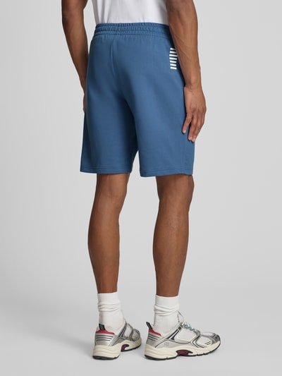 Männermodel trägt Sweatshorts mit Logo und Eingrifftaschen von EA7 Emporio Armani aus Reine Baumwolle, Regular-Fit, Ganzkörperansicht Rückansicht.