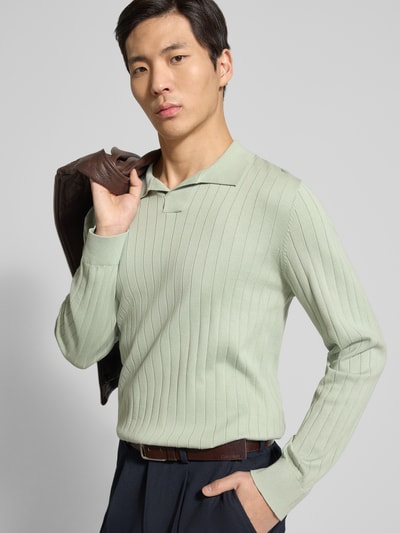 Mężczyznamodel nosi Loose Fit Poloshirt aus reiner Baumwolle Modell 'TORINO' von SELECTED HOMME, jasna zieleń, prążkowana tekstura, długi rękaw, klasyczny polokrag z V-dekoltem, detal na piersi, widok na górną część ciała z przodu.