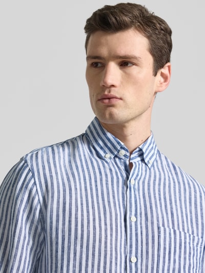 Męski model nosi Modern Fit Freizeithemd aus reinen Leinen Modell 'Daniel' od Brax w biało-niebieskie paski, koszula casualowa z kołnierzykiem typu button down i listwą guzikową, długość tyłu w rozmiarze M 76 cm, szerokość w rozmiarze M 50 cm, długość rękawów w rozmiarze M 67 cm, zbliżenie na górę torsu.