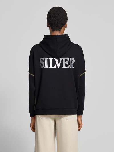Frauenmodel trägt Oversized Hoodie aus reiner Baumwolle Modell 'Silver and Gold' von miss goodlife in Schwarz mit Statement-Print, Ganzkörperansicht Rückansicht.