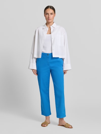 Vrouwenmodel draagt Slim Fit Chino uit katoenmix van Tommy Hilfiger, effen blauw, slim fit, met riemlussen en steekzakken, volledig frontaal lichaamsperspectief.