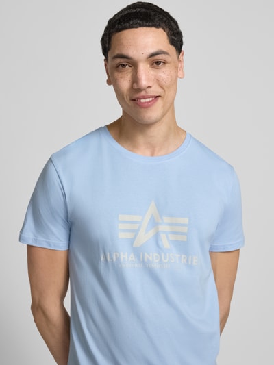 Męski model nosi t-shirt z bawełny, prosty krój, okrągły dekolt, detal z logo, model 'BASIC' od Alpha Industries, długość tyłu 69 cm, rozmiar M, jasnoniebieski, zbliżenie na górną część ciała