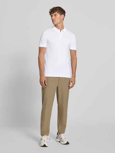 Mężczyzna nosi koszulkę polo Regular Fit Poloshirt aus reiner Baumwolle model 'PIO 1' od BOSS Green, kolor biały, gładka faktura, Ganzkörperansicht z przodu.