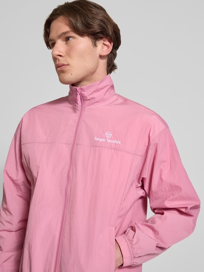 Männermodel trägt Regular Fit Jacke mit Stehkragen Modell 'Nayla' von SERGIO TACCHINI w kolorze różowym, wpuszczane kieszenie, zamek błyskawiczny, elastyczne wykończenia, długość tyłu 69 cm, długość rękawów 61 cm, krój regular fit, widok na górną część ciała z przodu.