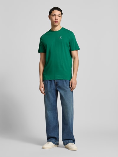 Männermodel trägt Regular Fit T-Shirt mit Logo-Print von Calvin Klein Jeans in Grün, reine Baumwolle, Rundhalsausschnitt, Ganzkörperansicht von vorne.