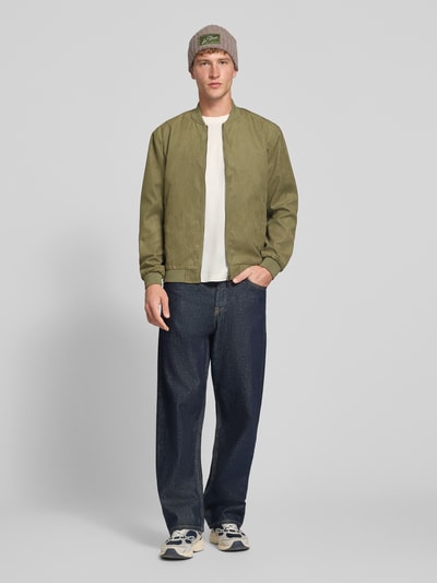 Männermodel trägt Regular Fit Blouson mit Baseball-Kragen Modell 'LUCAS' von ONLY, grün, kombiniert mit Jeans, Herren Bomberjacke / Blouson, Ganzkörperansicht von vorne.