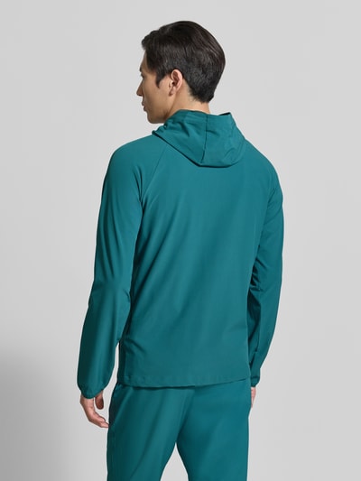 Männermodel trägt Regular Fit Jacke mit Logo-Print Modell 'Vibe' von Under Armour in Petrol, glattes Material, Rückansicht, Ganzkörperansicht. Elastischer Material-Mix, Kapuze, Reißverschluss, Eingrifftaschen, Rückenlänge 70 cm, Ärmellänge 72 cm.