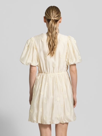 Frauenmodel trägt Minikleid mit V-Ausschnitt Modell 'CHAYA' von SUNCOO PARIS, cremefarben, Lyocell-Mix, Puffärmel, Wickel-Optik, Rückenlänge 89 cm, taillierte Passform, Ganzkörperansicht Rückansicht.