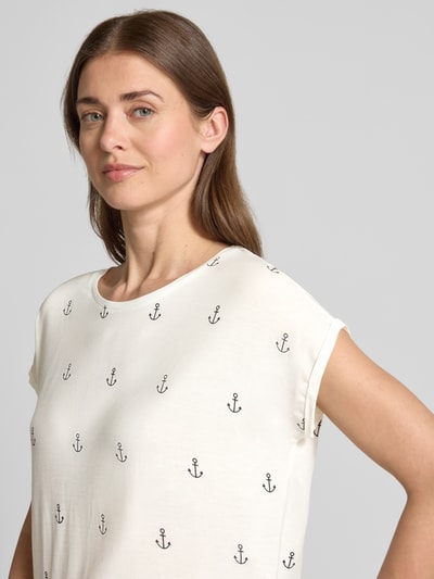 Frauenmodel trägt Relaxed Fit T-Shirt aus Lyocell-Mix Modell 'AVA' von Vero Moda, Optik:Allover-Muster mit Allover-Print, Kurzarm, Rundhals, Material Lyocell-Mix, weiße Grundfarbe mit schwarzen Ankern, glatte Textur, Nahaufnahme Oberkörper.