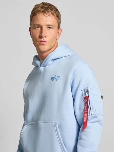 Männermodel trägt Hoodie mit Label-Details von Alpha Industries in Hellblau, Baumwoll-Mix, Lockerer-Schnitt, Nahaufnahme Oberkörper.