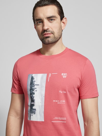 Męski model nosi Regular Fit T-Shirt aus reiner Baumwolle von Tom Tailor Denim, kolor różowy, nadruk z napisem i zdjęciem, krój regular fit, okrągły dekolt, krótki rękaw, tekstura gładka, widok na górną część ciała z przodu.