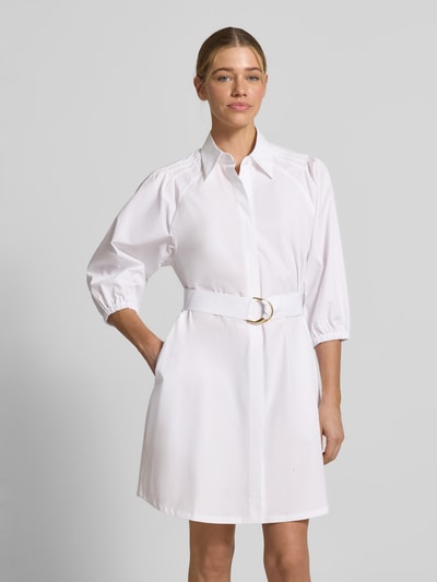 Frauenmodel trägt ausgestelltes, weißes Hemdblusenkleid aus reiner Baumwolle von HUGO, Modell 'KILONI', Bindegürtel, V-Ausschnitt, 3/4-Arm, Ganzkörperansicht von vorne.