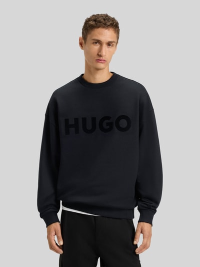 Männermodel trägt Oversized Sweatshirt aus reiner Baumwolle Modell 'DINEX' von HUGO in Schwarz, unifarben, Rundhals, Label Print, Ganzkörperansicht von vorne