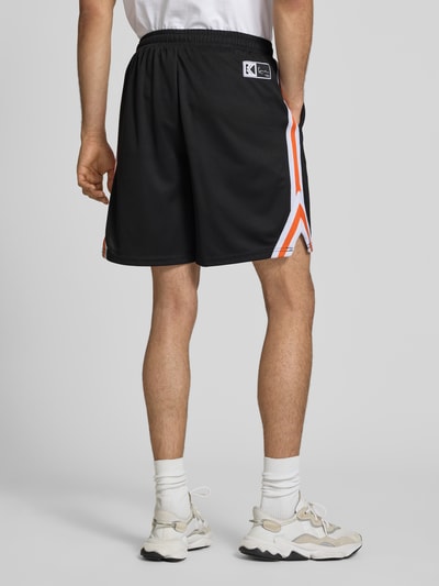 Männermodel trägt Regular Fit Shorts mit Logo-Print von KARL KANI in Schwarz mit Strukturmuster und elastischem Bund, Ganzkörperansicht Rückansicht.