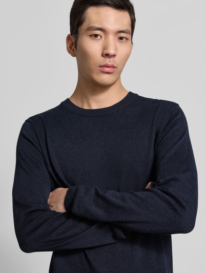 Męskamodel nosi granatowy Strickpullover mit gerippten Abschlüssen Modell 'BELLS' von Casual Friday z bawełniano-lyocellowej mieszanki, krój slim fit, okrągły dekolt, widoczne ściągacze, ujęcie z przodu górnej części ciała.