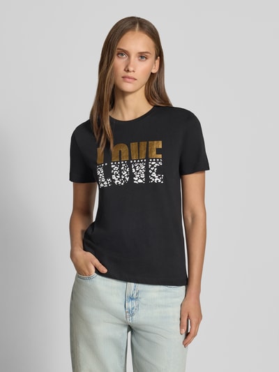 Mädchen trägt Regular Fit T-Shirt aus reiner Baumwolle Modell 'KITA' von ONLY, schwarz mit gold-weißem Print, Damski t-shirt, Damen T-Shirt von ONLY, Nahaufnahme Oberkörper
