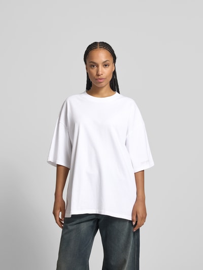 Frauenmodel trägt Oversized T-Shirt mit Label-Stitching von black palms aus reiner Baumwolle, Rundhalsausschnitt, Halbarm, weiß, Ganzkörperansicht von vorne.