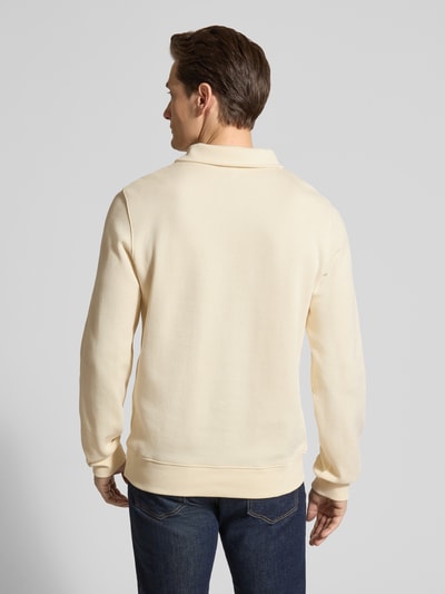 Męski model nosi Regular Fit Sweatshirt aus reiner Baumwolle von Lacoste, gładka tekstura, kolor kremowy, krój regular fit, logo, długi rękaw, kołnierzyk polo, bawełna, widok całej sylwetki z tyłu.