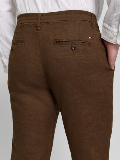 Männermodel trägt Regular Fit Leinenhose mit Logo-Stitching Modell 'Denton' van Tommy Hilfiger, bruine uni kleur, detailopname rugaanzicht.