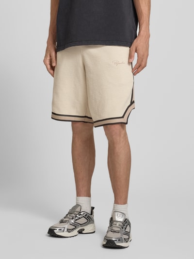 Männermodel trägt Shorts mit Strukturmuster und Label-Stitching von PEGADOR in Beige mit schwarzen Details, Regular-Fit, Reine Baumwolle, Eingrifftaschen, Elastischer Bund, Ganzkörperansicht von vorne.