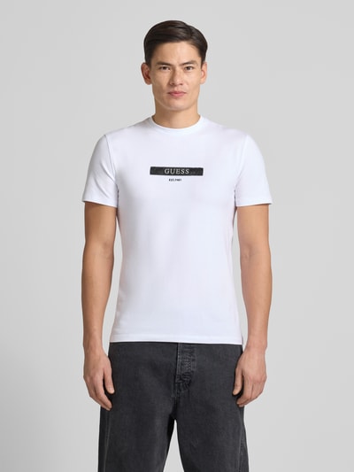 Männermodel trägt T-Shirt mit Label-Detail van Guess in wit, katoen-elastaan mix, regular fit, geribbelde ronde hals, Ganzkörperansicht von vorne.