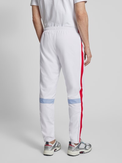 Männermodel trägt Regular Fit Trainingsanzug mit Kontraststreifen von Lacoste Sport, weiß mit roten und blauen Streifen, Ganzkörperansicht Rückansicht.