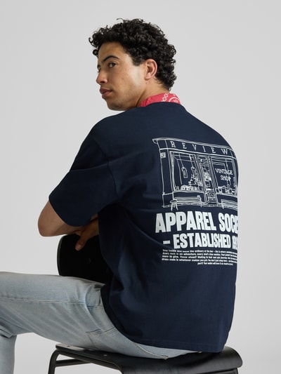 Männermodel trägt T-Shirt mit Rundhalsausschnitt und Logo-Print von REVIEW aus Reine Baumwolle Modern Fit, Rückenlänge 68 cm, Ganzkörperansicht Rückansicht.