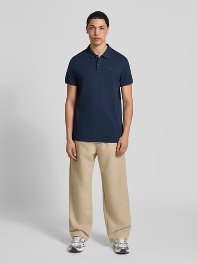 Mannenmodel draagt Regular Fit poloshirt model 'TJM SLIM PLACKET POLO EXT' van Tommy Jeans, look: effen, pasvorm: regular fit, applicatie: logostitching, polokraag, 2-knoopsluiting, materiaal: puur katoen, kleuren: donkerblauw, beige, grijs, wit. Volledige lichaamsaanzicht van voren.
