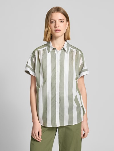 Frauenmodel trägt Regular Fit Bluse aus reiner Baumwolle von Brax in Two-Tone-Optik mit Streifenmuster, Hemdblusenkragen, einreihiger Knopfleiste und Kurzarm, Farben Olivgrün und Weiß, feine Baumwollstruktur, Ganzkörperansicht von vorne.