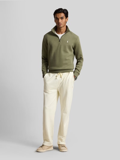 Männermodel trägt Relaxed Fit Troyer aus Baumwoll-Mix von Polo Ralph Lauren in Olivgrün, kombiniert mit heller Hose, Ganzkörperansicht von vorne.