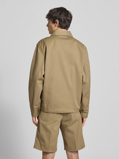 Męski model nosi Jacke mit Label-Stitching und Eingrifftaschen von Carhartt Work In Progress, kolor beżowy, krój regular fit, wykładany kołnierz, zamek błyskawiczny, wyhaftowane logo, wpuszczane kieszenie, długość tyłu w rozmiarze M: 68 cm, szerokość ramion w rozmiarze M: 59 cm, szerokość klatki piersiowej w rozmiarze M: 60 cm, długość rękawów w rozmiarze M: 20 cm, całkowity widok od tyłu