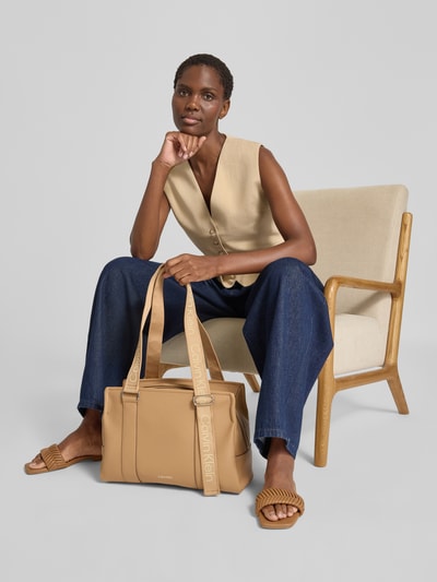 Vrouwenmodel draagt shopper van katoenmix van CK Calvin Klein in camel met lichte structuur, geheelopname vooraan.