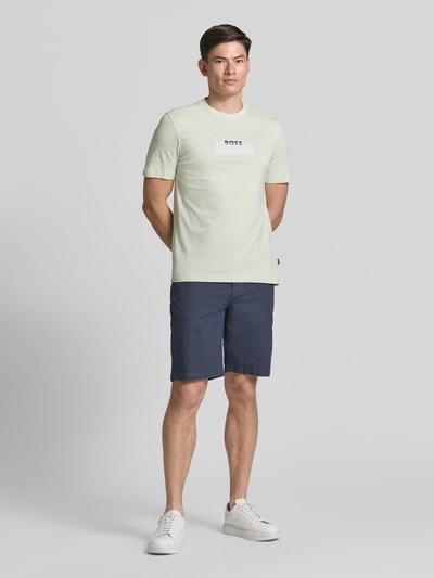 Männermodel trägt Tapered Chinoshorts aus Baumwoll-Mix Modell 'CHINO_TAPERED_DS_3S' von BOSS Orange, unifarben, Ganzkörperansicht von vorne.