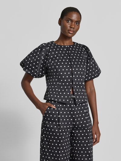 Frauenmodel trägt Slim Fit Bluse im Allover-Look Modell 'ANELA' von Neo Noir mit Rundhalsausschnitt und Puffärmeln, Nahaufnahme Oberkörper. Damen Bluse, Hakenverschluss, Rückenlänge 48 cm, Ärmellänge 30 cm, schwarze Grundfarbe mit weißen Punkten, glatte Textur.
