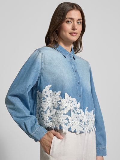 Frauenmodel trägt Regular Fit Hemdbluse in Denim-Optik mit Spitzenbesatz von More & More aus reiner Baumwolle, hellblaue Farbe, weiße Spitzenverzierung, durchgängige Knopfleiste, Hemdblusenkragen, langärmlig, glatte Textur, Nahaufnahme Oberkörper.