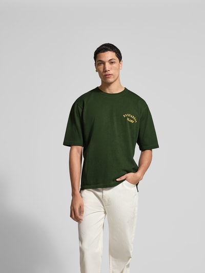 Männermodel trägt Loose Fit T-Shirt aus reiner Baumwolle von Dsquared2 in Dunkelgrün mit Label-Print, Rundhalsausschnitt, Kurzärmelig, Rückenlänge 68 cm bei Größe M, Ganzkörperansicht von vorne.