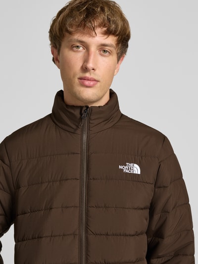 Männermodel trägt Regular Fit Jacke in Stepp-Optik Modell 'ACONCAGUA' von The North Face, braun, Reißverschluss, Logo-Stitching, Nahaufnahme Oberkörper.