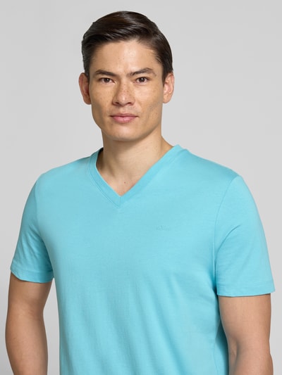 Męski model nosi Regular Fit T-Shirt aus reiner Baumwolle od s.Oliver RED LABEL, jednokolorowy, krój regular fit, aplikacja z metką, dekolt w serek, krótki rękaw, dżersej, czysta bawełna, jasnoniebieski kolor, gładka faktura, zbliżenie na górną część ciała, widok z przodu.