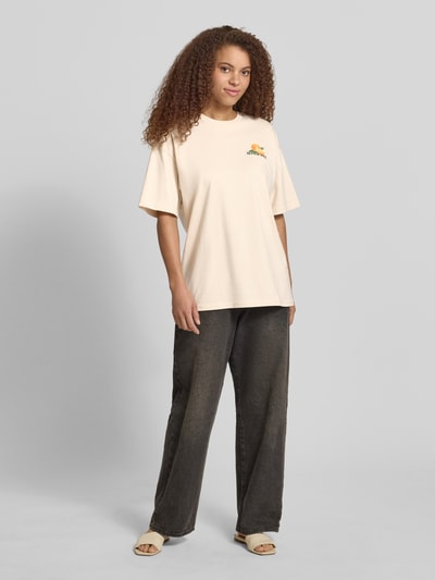 Frauenmodel trägt T-Shirt mit rückseitigem Motiv-Print von REVIEW aus Reine Baumwolle, Oversized, Rundhalsausschnitt, Damen T-Shirt, Rückenlänge 68 cm, helle Farbe, glatte Textur, Ganzkörperansicht von vorne.