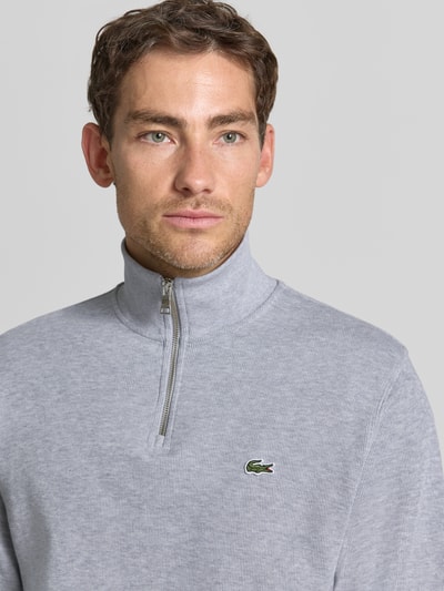 Männermodel trägt Regular Fit Troyer aus reiner Baumwolle von Lacoste in Hellgrau, dezente Struktur, Nahaufnahme Oberkörper, Herren Troyer von Lacoste.