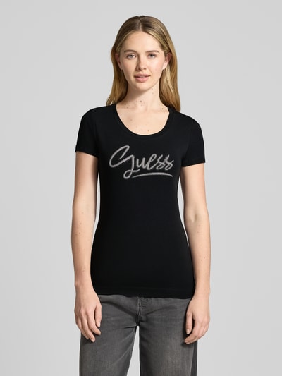 Vrouwenmodel draagt Slim Fit T-Shirt met Strasssteinbesatz van Guess in zwart, rondhals, logo in steentjes, elastische katoenmix, geheel vooraanzicht.