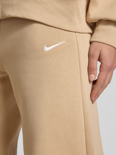 Frauenmodel trägt Wide Leg Sweatpants mit Logo Modell 'Phoenix' von Nike aus Baumwoll-Mix, Beige, Logo, Nahaufnahme Oberschenkel. Damen Sweatpants, elastischer Bund, Tunnelzug, Innenbeinlänge 78 cm bei Größe S.