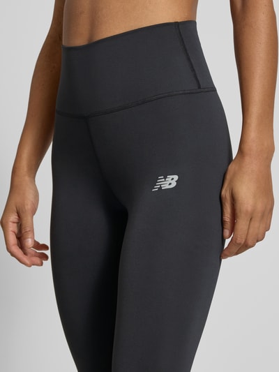 Frauenmodel trägt Leggings mit Label-Print Modell 'Harmony' von New Balance, hoher Bund, elastischer Stoff, dunkle Farbe, Nahaufnahme Oberkörper.