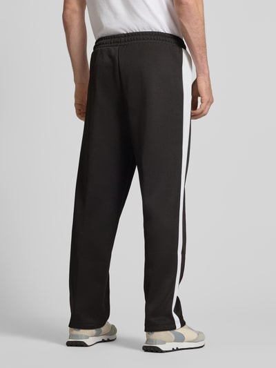 Männermodel trägt Straight Fit Sweatpants mit Logo-Stitching Modell 'Always On' von PUMA PERFORMANCE, Schwarz mit weißen Seitenstreifen, Material-Mix mit Baumwoll-Anteil, Ziernähte, elastischer Bund, Reißverschluss-Eingrifftaschen, Innenbeinlänge bei Größe M 75 cm, Ganzkörperansicht Rückansicht.