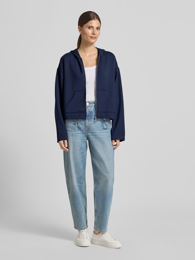 Modelka nosi Regular Fit Sweatjacke mit Kapuze von Christian Berg Woman, elastyczna mieszanka materiałów z domieszką modalu, kieszeń kangurka, pas z tunelem, krój regular fit, widok całej sylwetki z przodu.