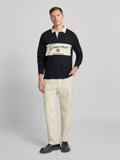 Männermodel trägt Sweatshirt mit Polokragen und verdeckter Knopfleiste von Gant in dunklem Blau und Beige, Reine Baumwolle, Regular-Fit, Label-Stitching, Rückenlänge 69 cm, Ärmellänge 66 cm, Ganzkörperansicht von vorne.