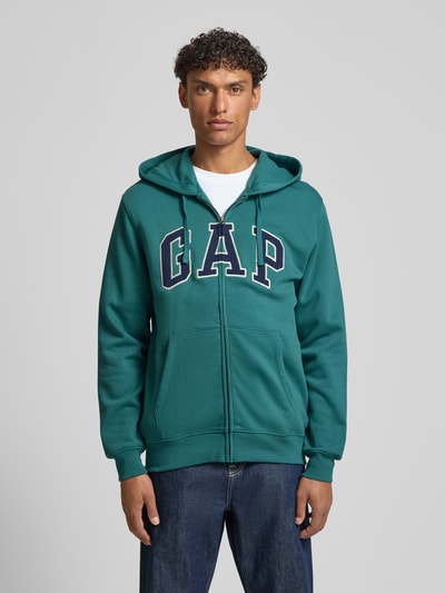 Männermodel trägt Sweatjacke mit Logo und Känguru-Tasche von GAP in Grün, Baumwoll-Mix, Regular Fit, Ganzkörperansicht von vorne.